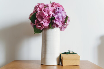 Hydrangea bouquet in vase and gift box on background of white wall with copy space. Beautiful pink and purple hydrangea flowers at home. Happy mothers day