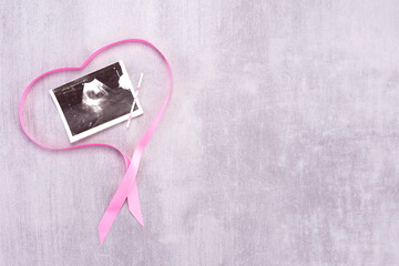 Ultrasound image of a baby with a pink ribbon in the form of a heart on a gray background with...