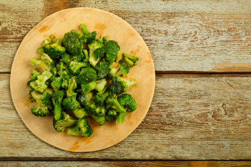 Scattered frozen broccoli on a round wooden board.