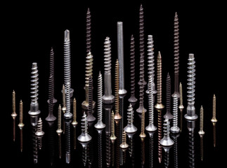 Metal screws, various sizes and views, with different lengths and threads, on a black background, selective focus.