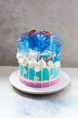 Blue winter cake with white chocolate, lollipops and fondant snowflakes. Grey background.