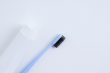 Blue toothbrush with black bristles and tube with toothpaste on a white background.
