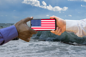Close up of afroamerican and caucasian white hands holding the phone with US flag in front of the...
