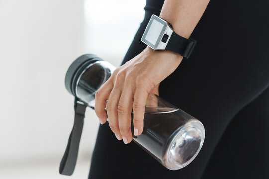 emale hand with smartwatch holding reusable bottle with water.