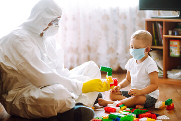 Man in protective hazmat suit plays constructor with little child in medical mask. The concept of...
