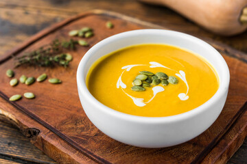 Pumpkin butternut squash cream soup in a bowl against wooden background - obrazy, fototapety, plakaty