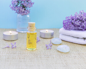 Fototapeta na wymiar Spa with lilac flowers. A bottle of scented oil, candles, and a napkin. Selective focus