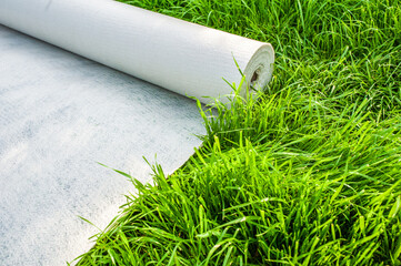 A roll of white geotextile lies on the green grass outside
