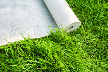 A roll of white geotextile lies on the green grass outside
