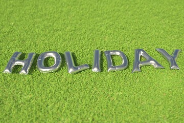 HOLIDAY word made with silver foil balloons on green grass