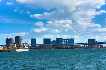 Fototapeta premium Boat moored on the shores of Tokyo Bay in front of the double-layered Rainbow Bridge with the bay of Odaiba and mall buildings in the background.