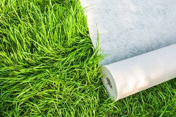 A roll of white geotextile lies on the green grass outside