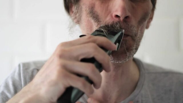 Middle-aged man shaves off mustache and long beard remnants on right face side