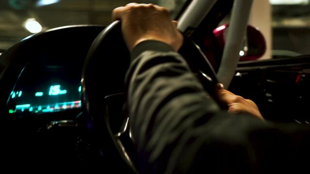 View inside of a car and the driving man. Footage. Close up of driver hands on the steering wheel of a car that is passing on underground parking.