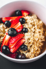 Close up view on oatmeal with strawberries and blueberries on bright textured table