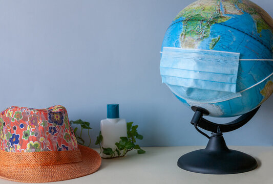 An anti-virus mask is worn on a globe, a woman's hat, a sanitizer in ivy leaves on a light background.