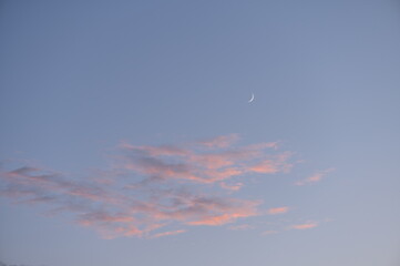 Rosa beleuchtete Wolken am Himmel am Abend leuchten mit Mondsichel (Neumond)