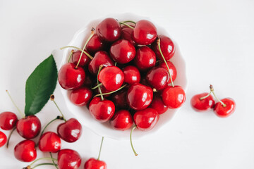 Naklejka na ściany i meble Fresh juicy red cherries in a white plate on the white wooden background. Top view. Copy, empty space for text