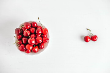 Fresh juicy red cherries in a white plate on the white wooden background. Top view. Copy, empty space for text