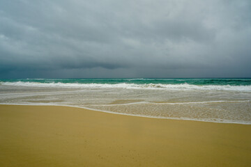 View from sandy beach across breaking waves to a stormy sky at Flinders Beach, North Stradbroke Island, Queensland, Australia.