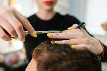 Hairdresser performs a men's haircut. Beautiful female with red lips cuts a man in the salon.