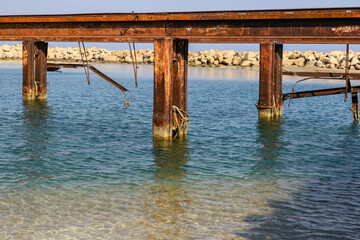 Rusting metal supports standing in clear blue Mediterranean water is all that remains of an old pier near Famagusta in Northern Cyprus.  A white sandy beach is in the background.