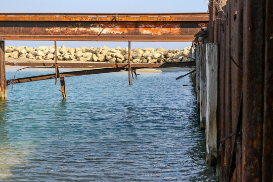 Rusting metal supports standing in clear blue Mediterranean water is all that remains of an old pier near Famagusta in Northern Cyprus.  A white sandy beach is in the background.