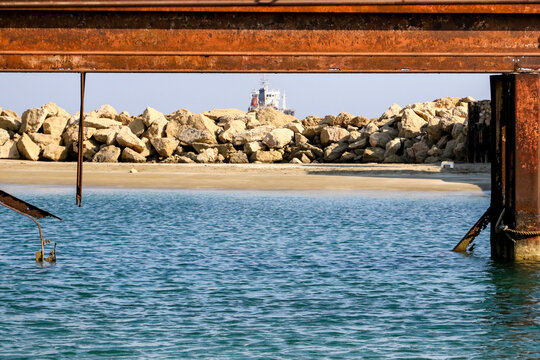 Rusting metal supports standing in clear blue Mediterranean water is all that remains of an old pier near Famagusta in Northern Cyprus.  A white sandy beach is in the background.