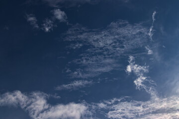 Naklejka na ściany i meble small tufts of white cloud, floating together under a dark blue sky.