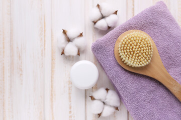 A lilac Terry towel, a white jar of cream, and cotton flowers on a wooden painted white background.Selective focus.Spa and dry massage. Body skin care. Fight against cellulite.Copy space