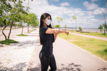 Jovem mulher se aquece e usa uma máscara para proteção.