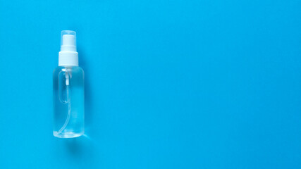 Hand sanitizer transparent bottle with spray cap at the left of blue background. Simple flat lay with copy space. Pastel paper texture. Medical concept. Stock photo.
