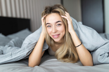 Smiling woman under a duvet in her bedroom. Closeup portrait of a beautiful young woman under the blanket. happy good morning