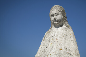 Obraz premium Virgin Mary ancient stone statue against blue sky
