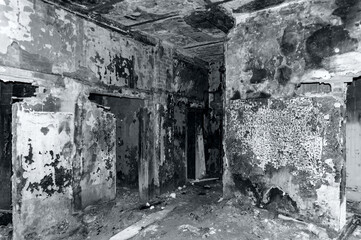 Abandoned ruined house, empty windows, charred walls, trash on the floor. Black and white photography.