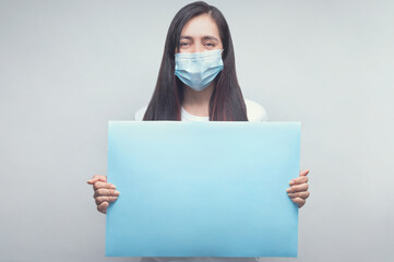 Woman portrait in inspirational mood with face mask and blue sign, physycal distancing.