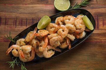 hrimp with garlic and oil, served on a dark plate on a rustic wooden table,
