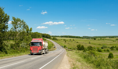 A truck with a tank on the road through the field on a sunny day.