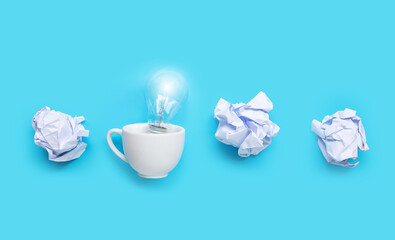 Light bulb in white cup with white crumpled paper balls on blue background. Ideas and creative...