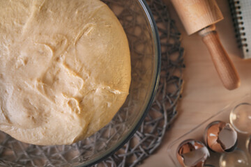 Naturally leavened sourdough dough in a glass bowl, wooden rolling pin, eggshells and a recipe book - flat lay photo.