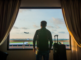 A young man with luggage is watching the take-off of the plane and then landing on the airplane.