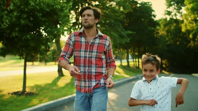 Positive Man And Boy Walking On Street. Happy Father And Son Dancing Outdoors