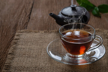 Hot organic teacup with kettle and green tea leaf on sack and wooden table background.