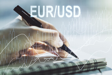 Creative concept of EURO USD financial chart illustration and woman hand writing in notebook on background. Trading and currency concept. Multiexposure