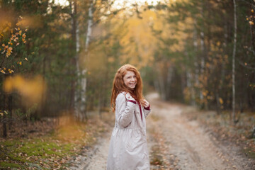 Fototapeta na wymiar Portrait of a happy cute red-haired child girl with freckles in a colorful autumn forest or park. Autumn mood.