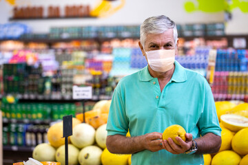 Handsome man posing using mask, looking at camera and holding melon in hand. Bearded customer smiling. Section with fresh citruses on background