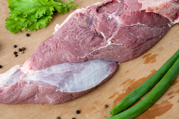 A piece of raw beef meat, lettuce leaf with green onions and black pepper peas on a wooden background