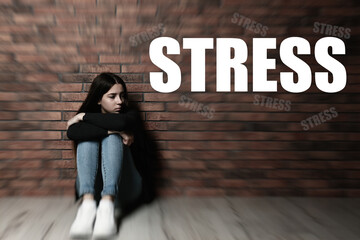 Word STRESS and depressed young girl sitting on floor near brick wall