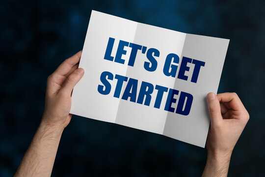 Man holding brochure with phrase LET'S GET STARTED on dark blue background, closeup