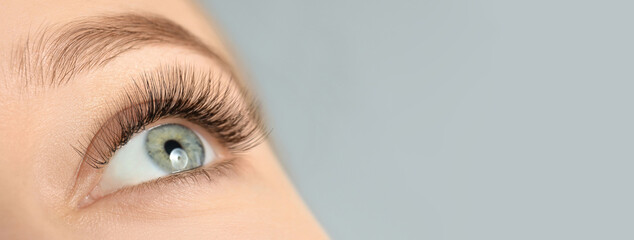 Closeup view of young woman with beautiful long eyelashes on grey background, space for text....